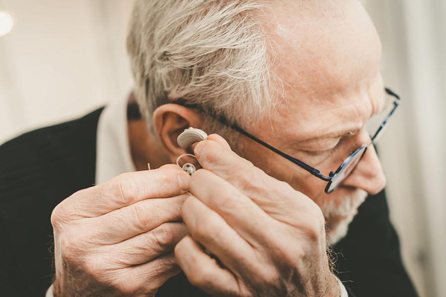 Older man placing a hearing aid in his ear.